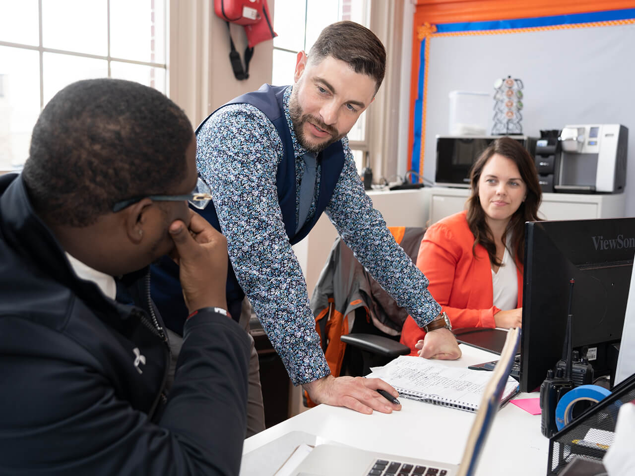 Three people collaborate at desks in an office setting.