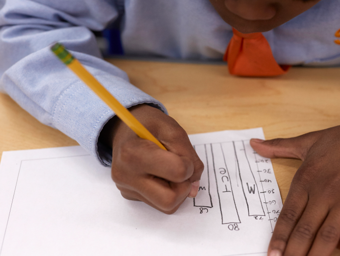 Child drawing graph on paper at classroom desk.