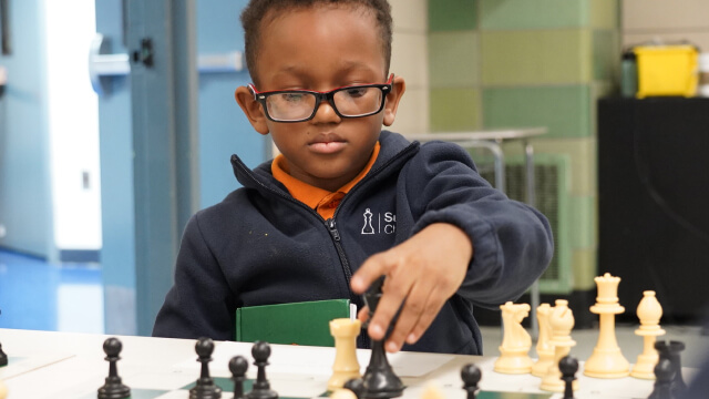 Child playing chess in classroom, focused expression, colorful walls.