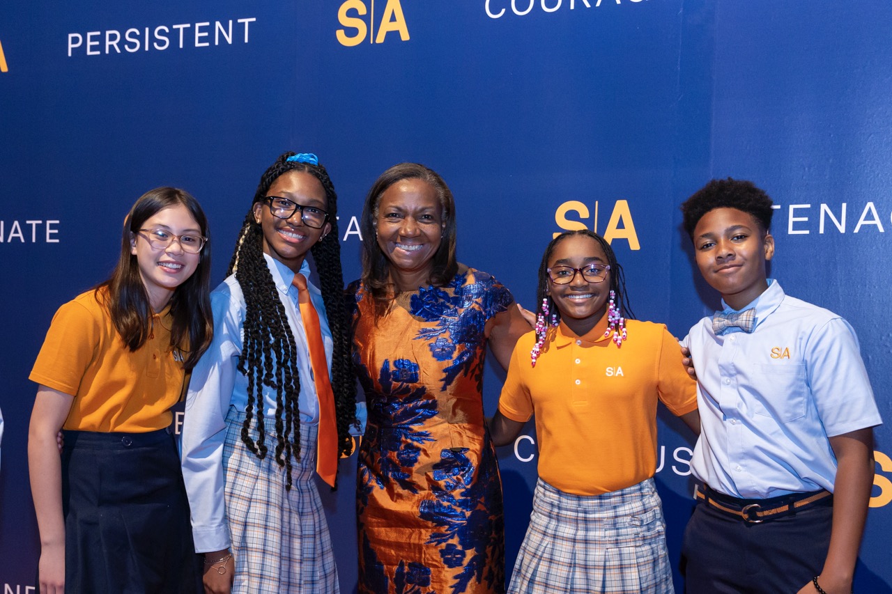 Group smiling, standing against blue wall with motivational words: 