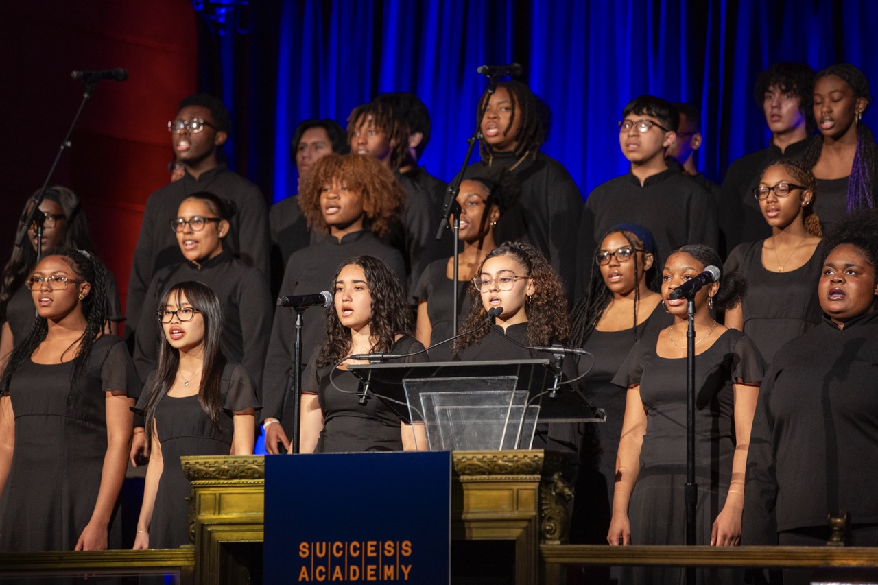 Chorus singing together on stage; blue curtain background.